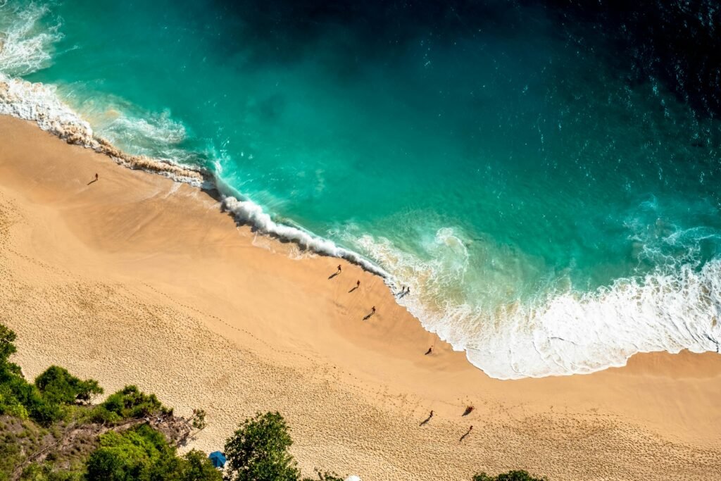 Stunning aerial view of Bali's beach with turquoise waves crashing on golden sand.